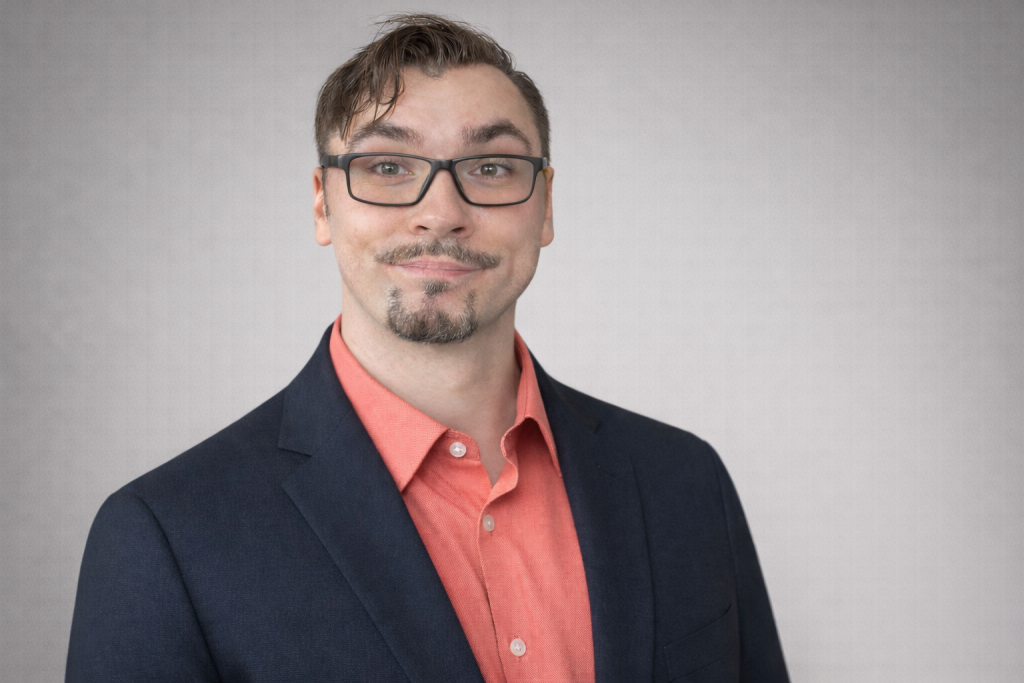 Ivan Popov headshot. He is wearing glasses, a salmon colored button up dress shirt and a black blazer.