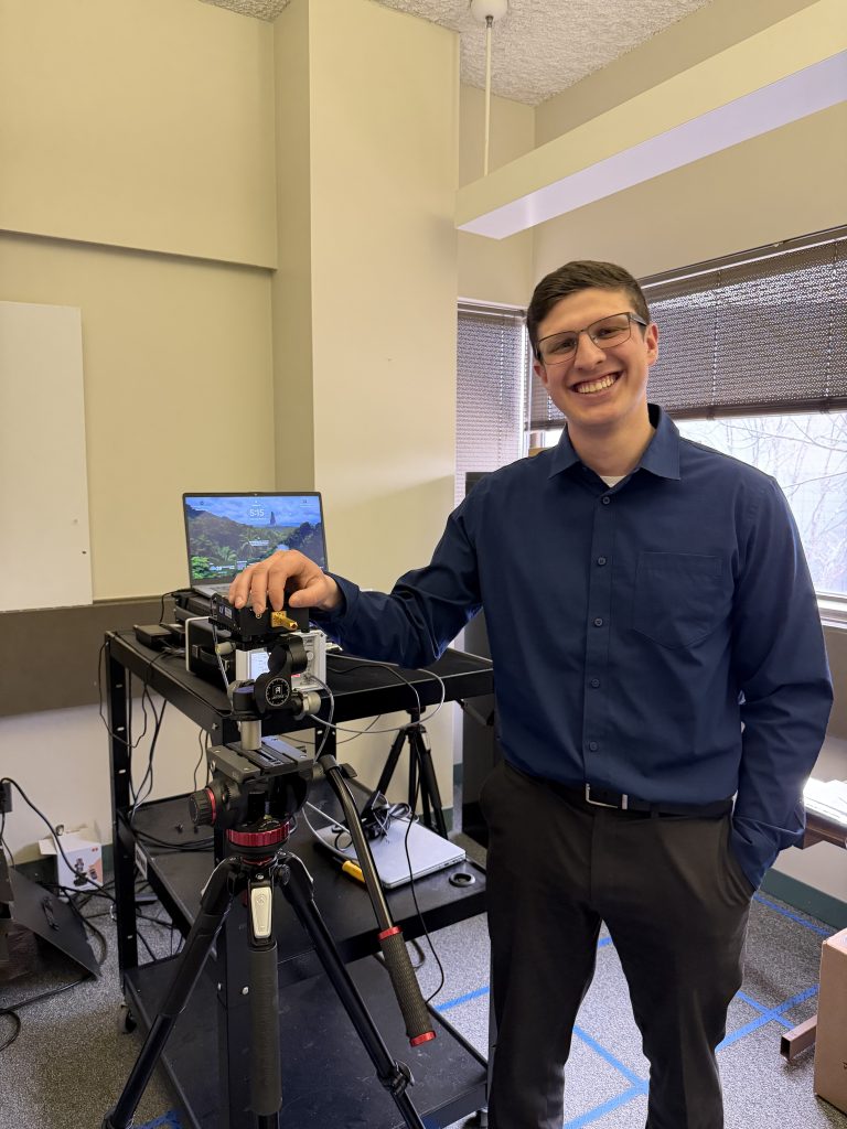 John Pertell in the Electrical and Computer Science Lab with a communications measuring device. He is wearing a navy dress shirt and dark slacks. He also has on glasses.