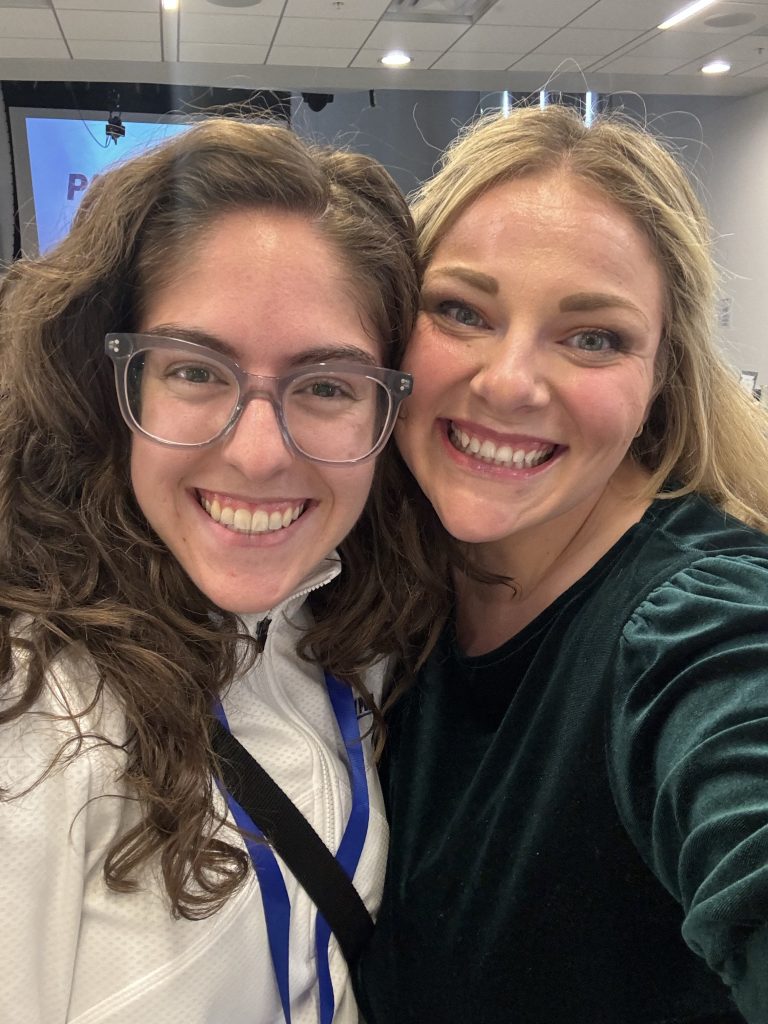 Carly Pimpnella wearing a white athletic sweater and clear glasses, next to mentor Alyssa Steele, who is wearing a green long sleeve blouse. 