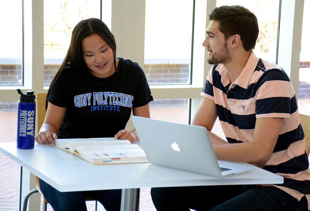 two students studying at a small table with a laptop